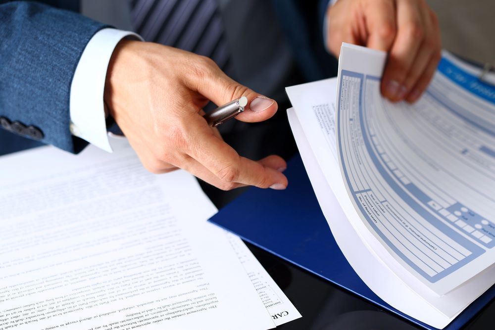 Image of a male arm in a suit offering an insurance form clipped to a pad, featuring 411 Immigration Law and highlighting Post-Approval Support, ensuring it aligns with the page's context.